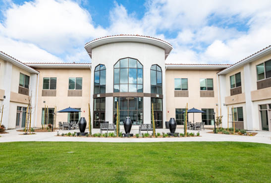 A large building with a circular window and a blue awning. The building has a grassy area in front of it. AI generated content