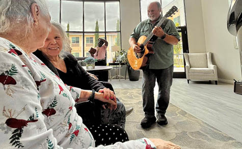 A man is playing a guitar while three women sit and watch. AI generated content