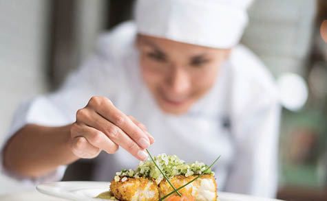Cook decorating a plate and putting the ultimate touches - focus on foreground 